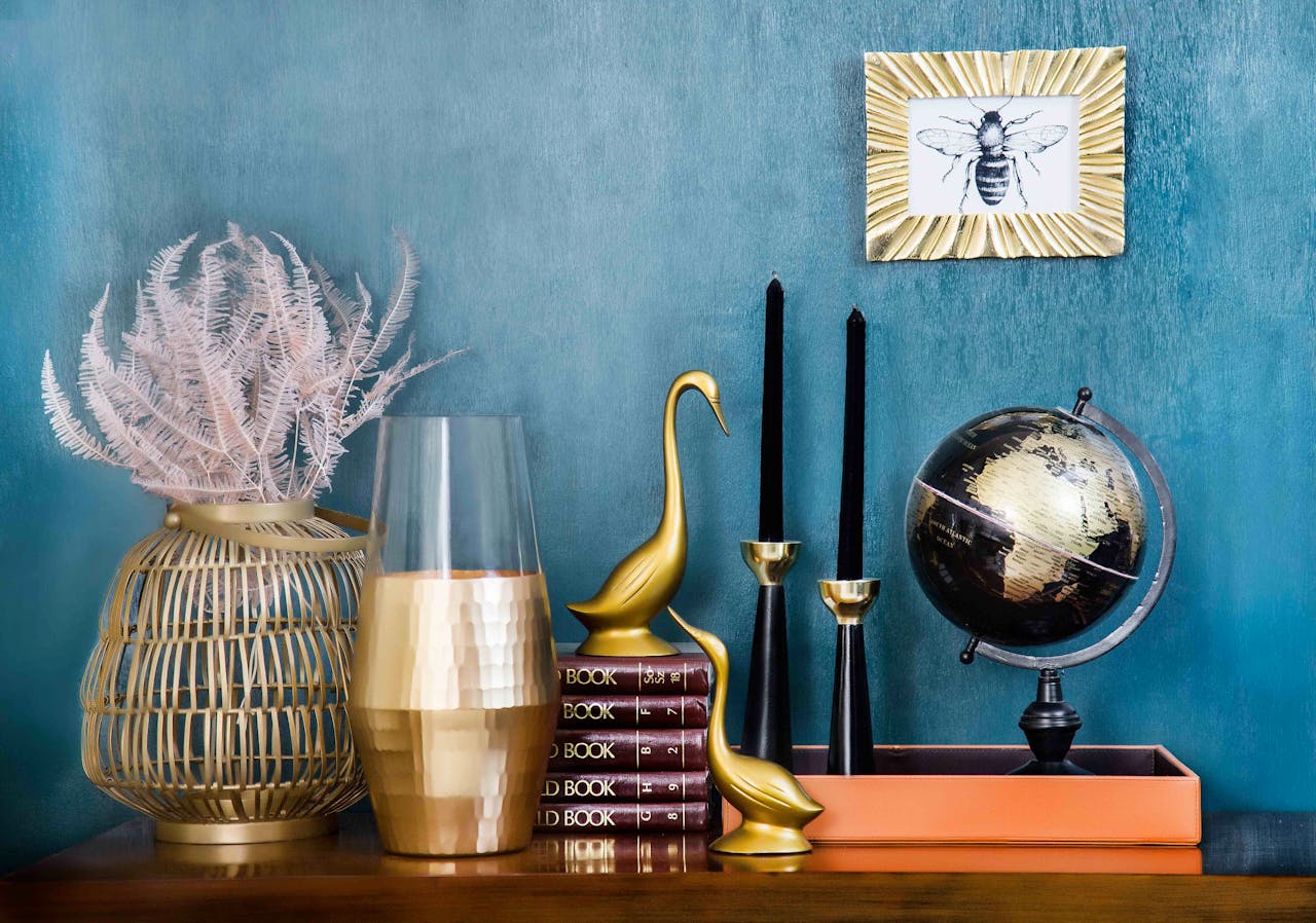 creative-03 Stylish home decor arrangement including a globe, books, candles, and vases on a blue backdrop.